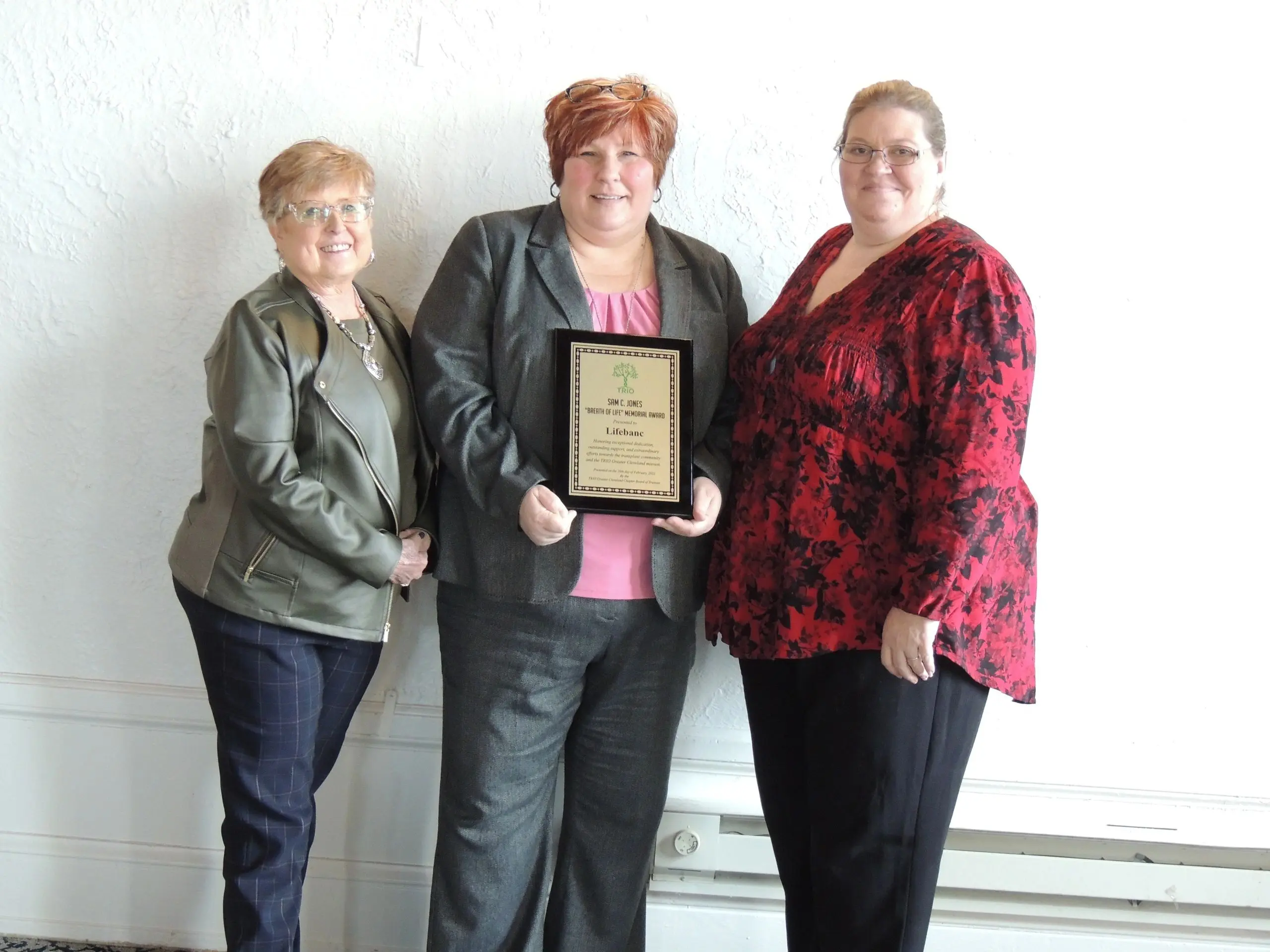 Women smiling while holding a recognition plaque.