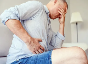 Man holding his side with one hand and the other hand is over his eyes. Showing pain and discomfort.